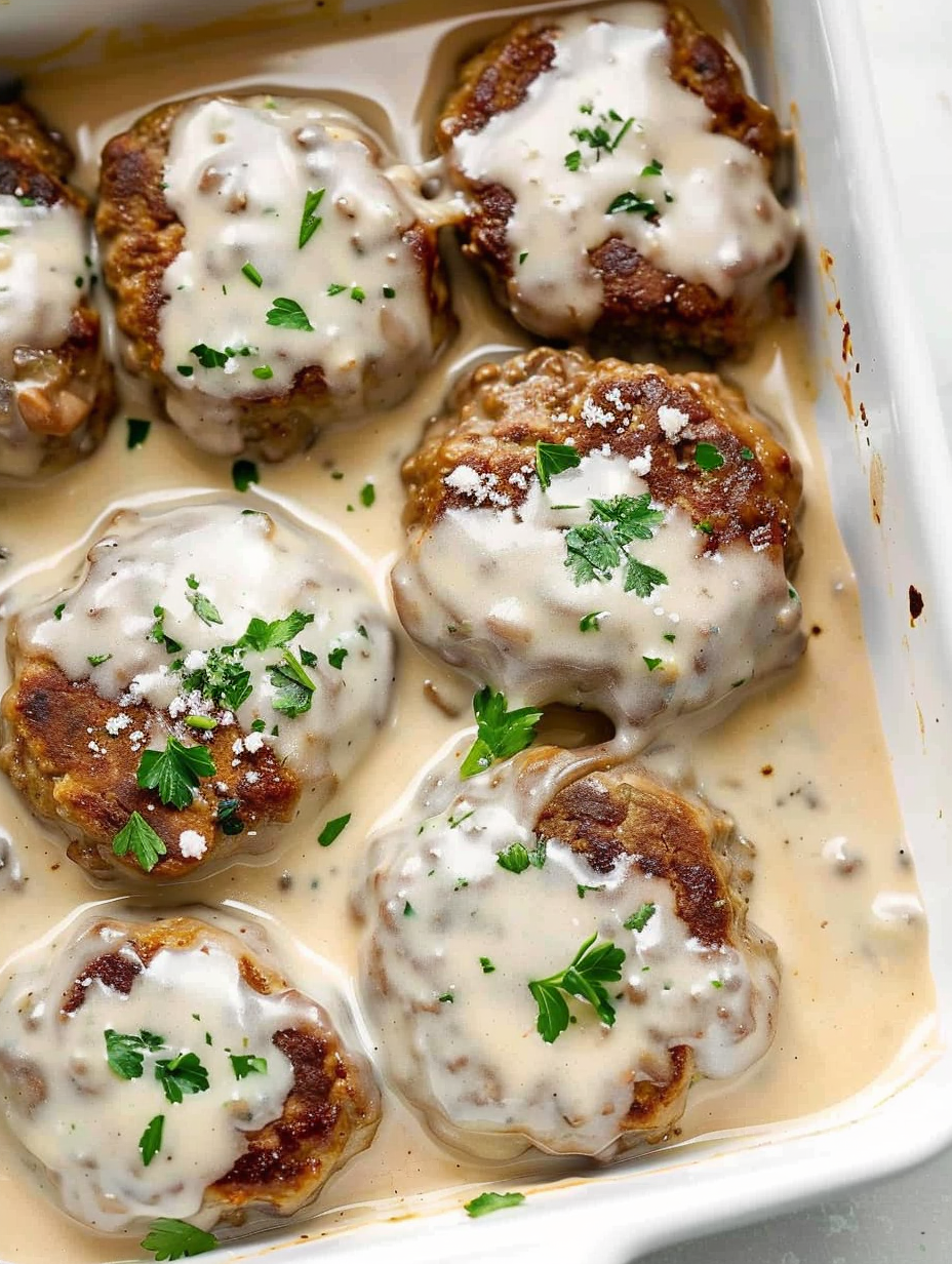 Seared hamburger patties arranged in a baking dish with creamy mushroom sauce