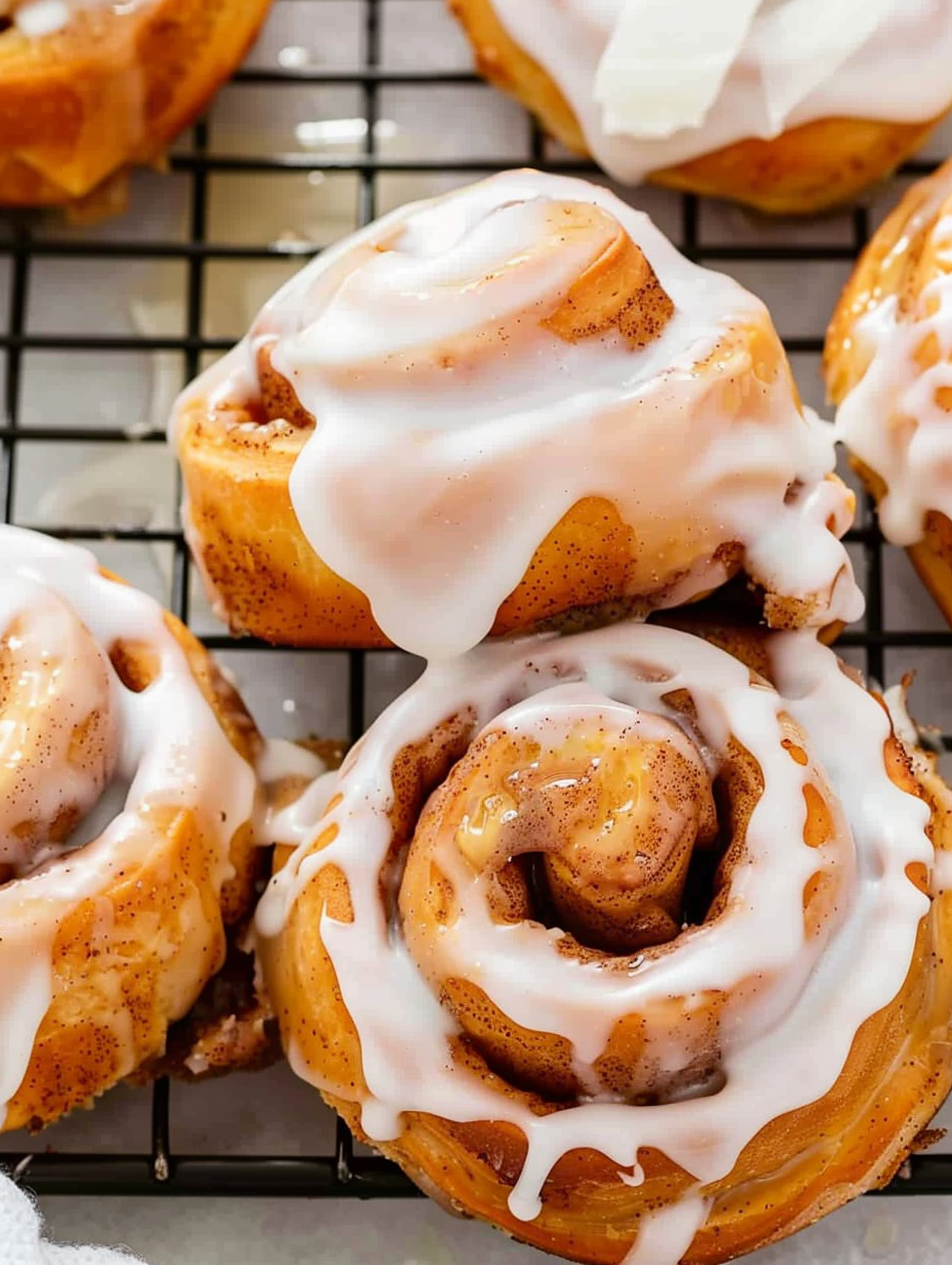 Fried cinnamon rolls drained on a rack and being glazed