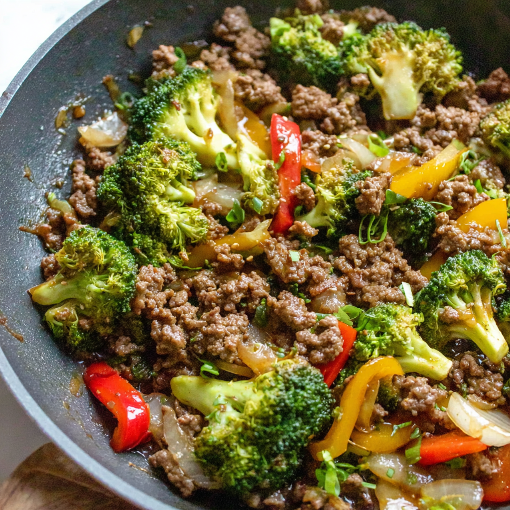 Skillet on stovetop with ground beef, peppers, and broccoli simmering