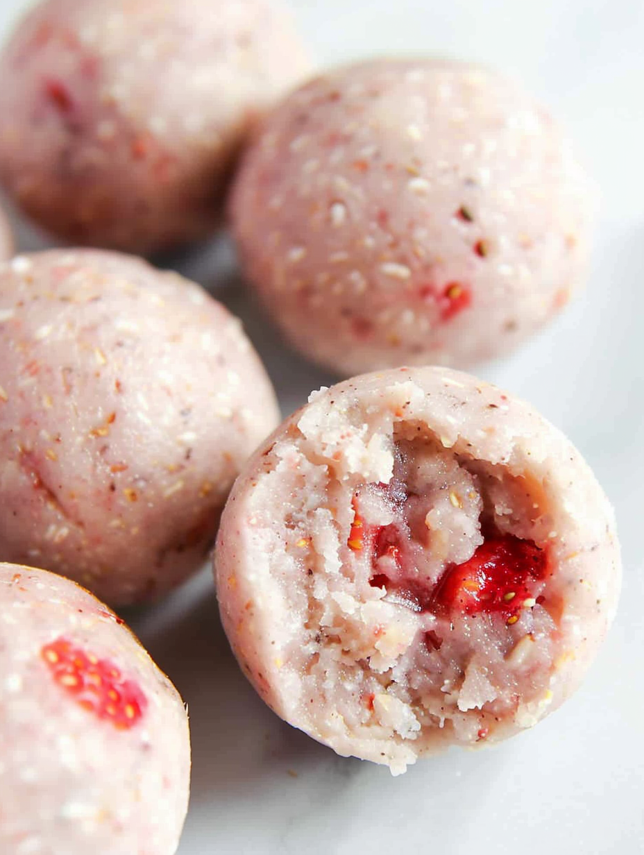 Three small pink strawberry protein balls on a white plate