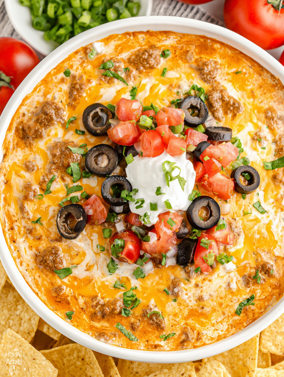 Serving bowl of cheesy taco dip with fresh toppings