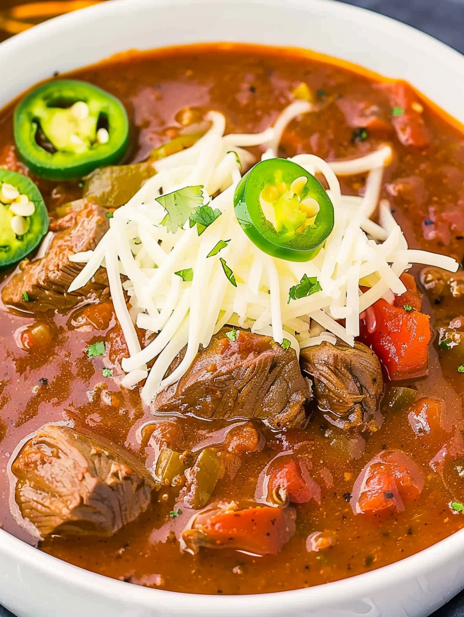 Bowl of Texas chili with chunks of beef and garnishes