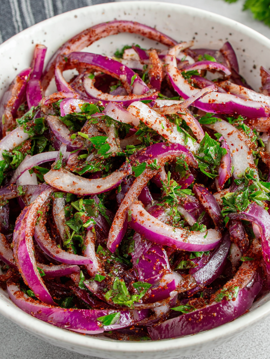 Thinly sliced red onions tossed with sumac and parsley in a bowl