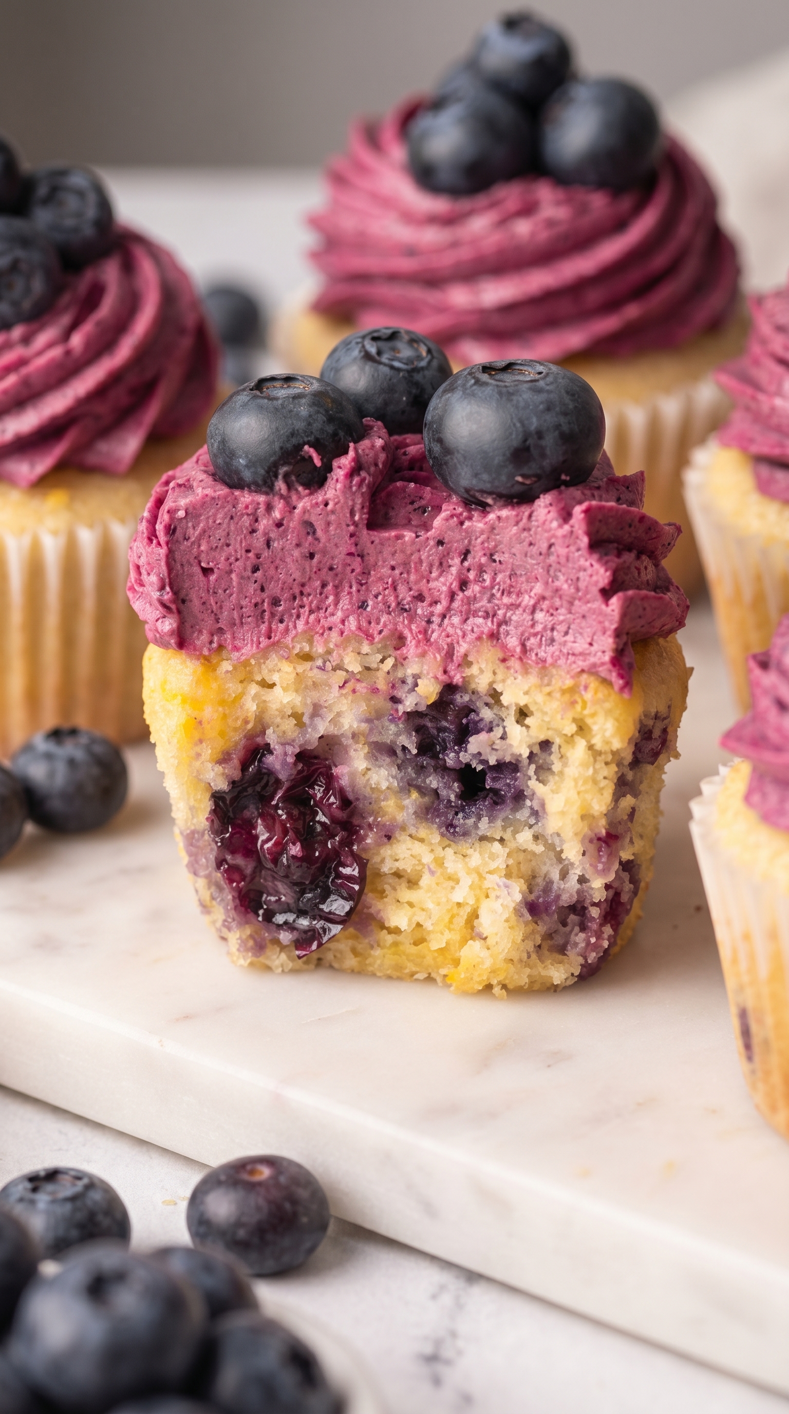 Vegan lemon blueberry cupcakes on a cooling rack with fresh blueberries