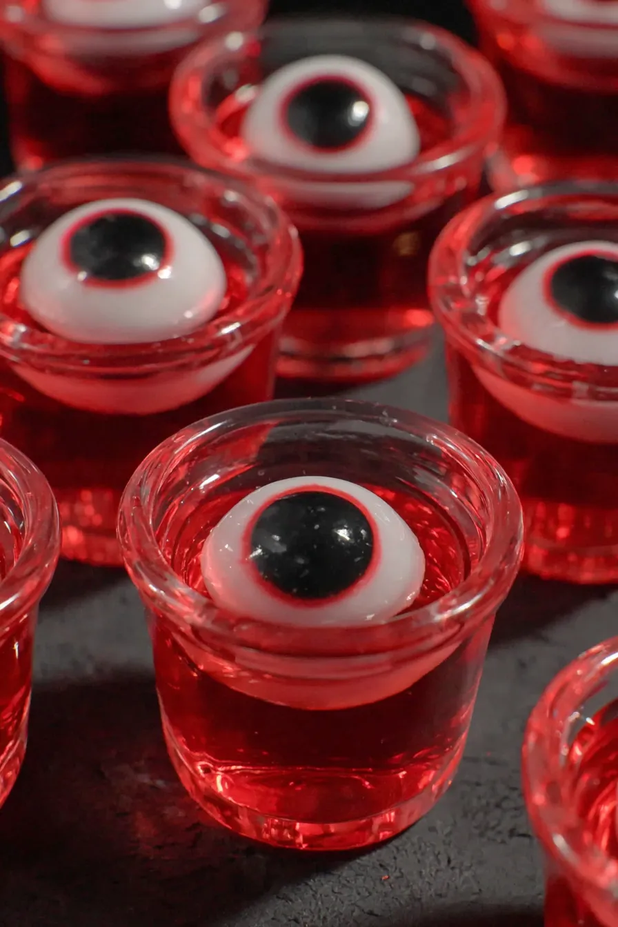 Close-up of red jello shots in clear shot glasses topped with candy eyeballs
