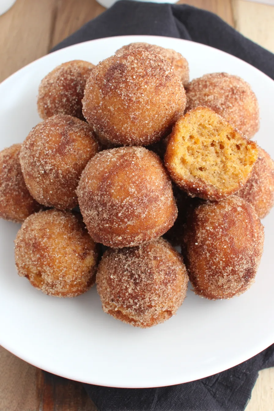 Tray of warm baked pumpkin donut holes being rolled in cinnamon sugar