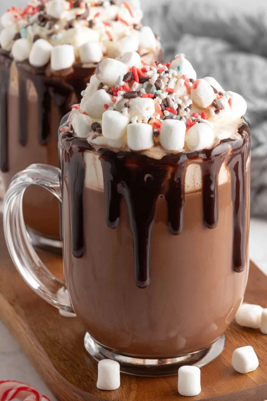 Mugs of creamy hot chocolate topped with marshmallows and cinnamon sticks