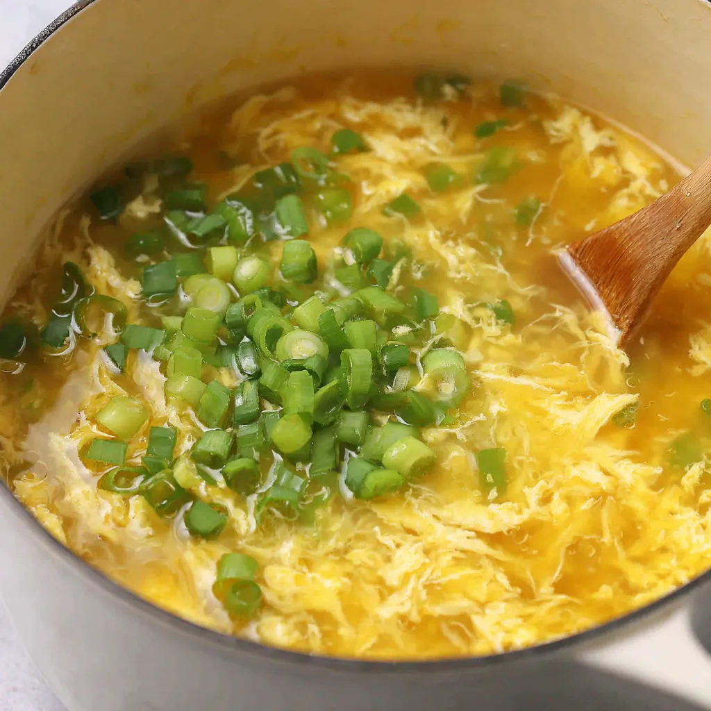 Serving egg drop soup with chili oil and scallions on a table