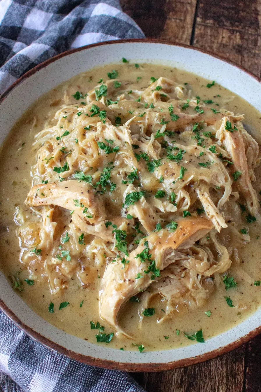 Slow cooker chicken and gravy in a white bowl with parsley