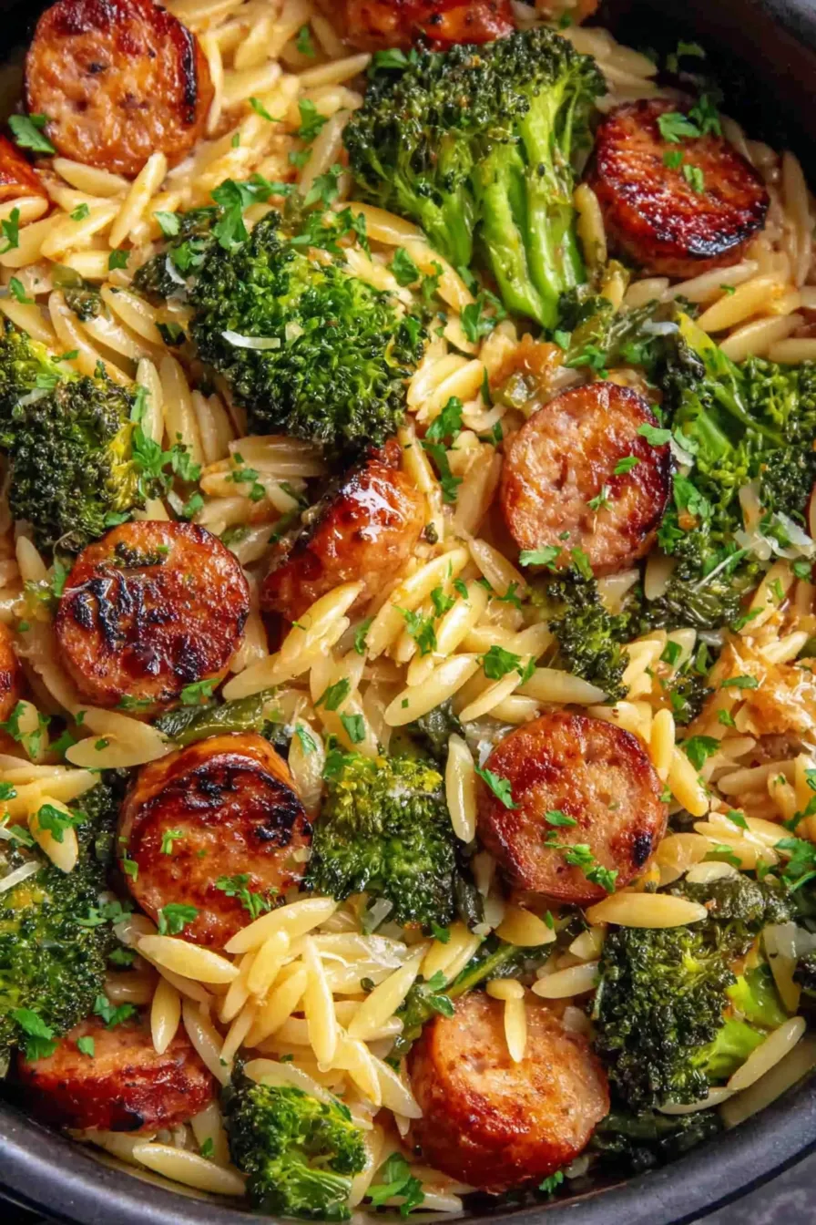 Sliced chicken sausage and broccoli artfully plated with orzo and parsley garnish