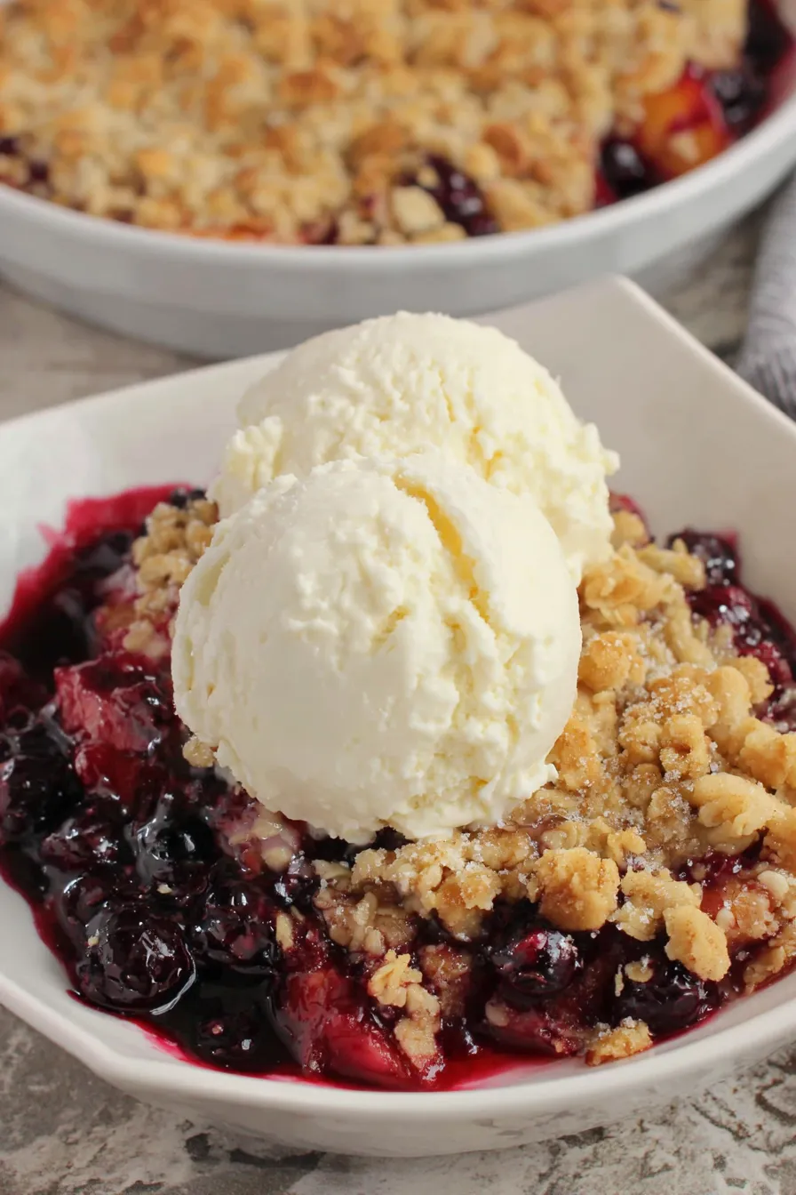 Two bowls of blueberry peach crisp served with vanilla ice cream