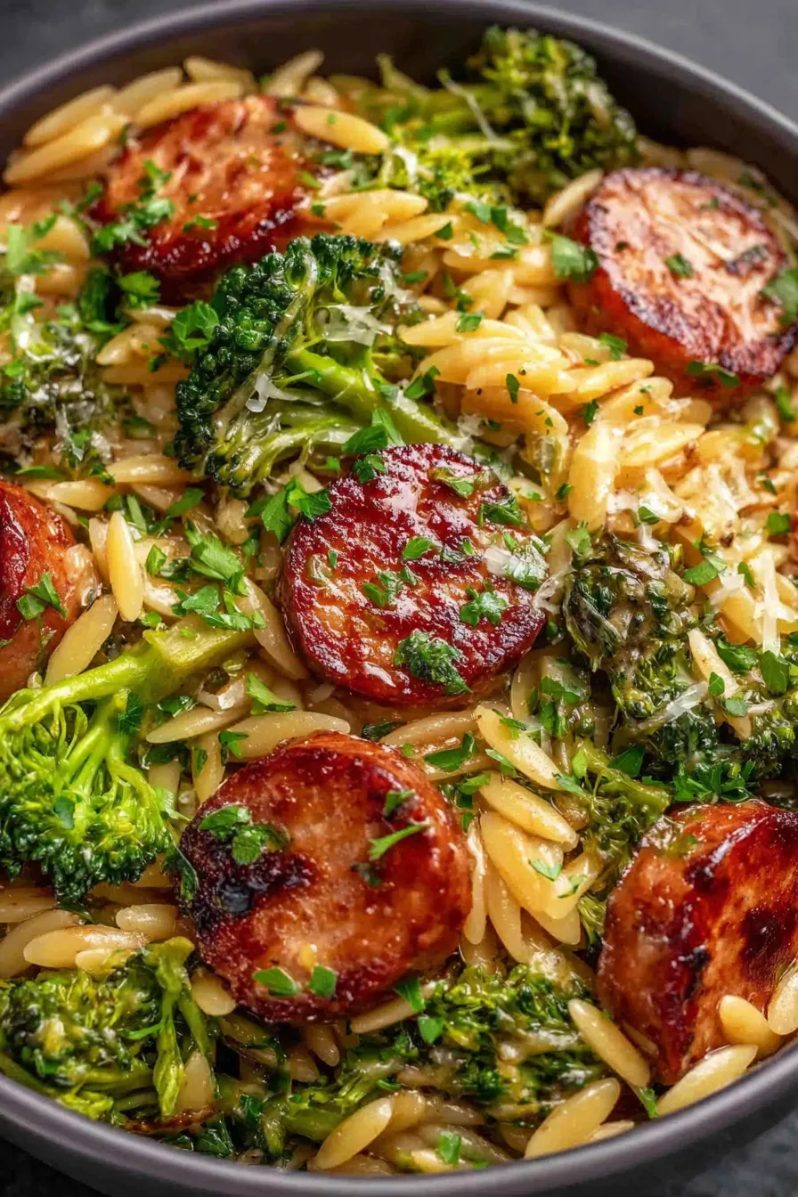 Close-up of orzo, broccoli, and sliced chicken sausage plated and garnished with parsley